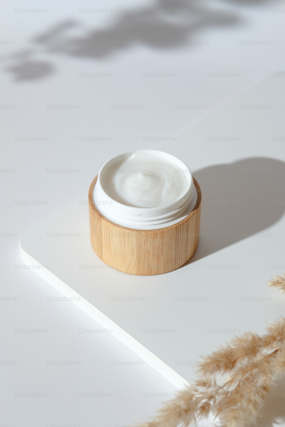Jar of natural organic cream moisturizer on white podium with dried flowers. Bio cosmetics in eco friendly bamboo packaging