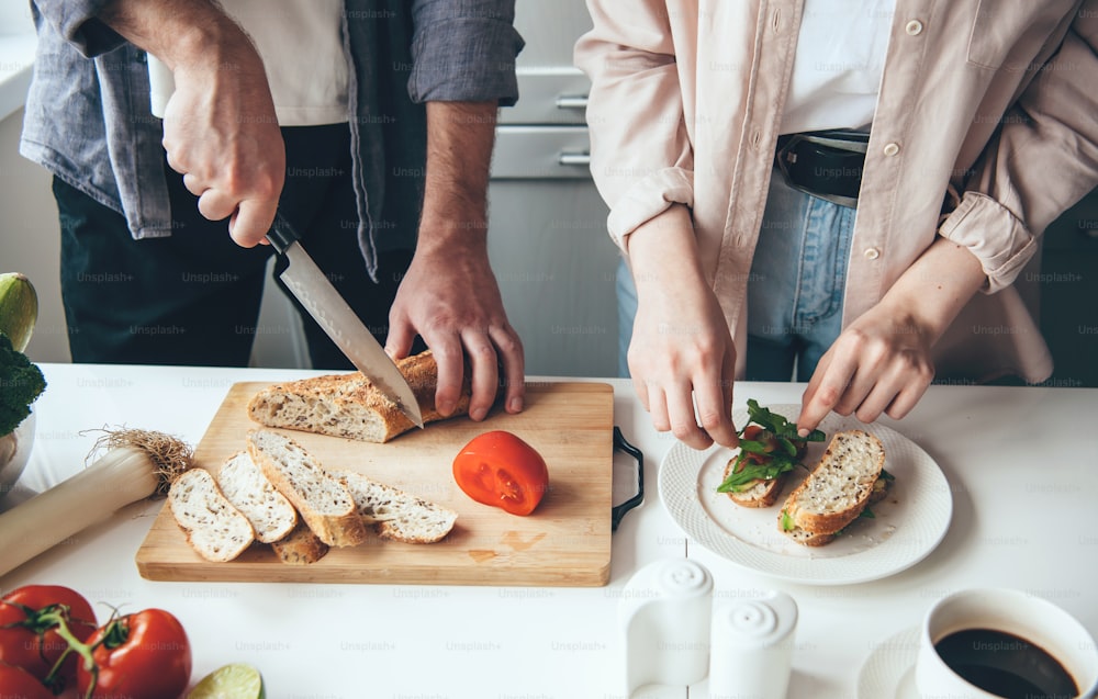 Caucasian couple preparing sandwiches together while slicing bread and vegetables in the kitchen