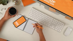 Top view of man writing on notebook while holding coffee cup with mock up smartphone, include clipping path