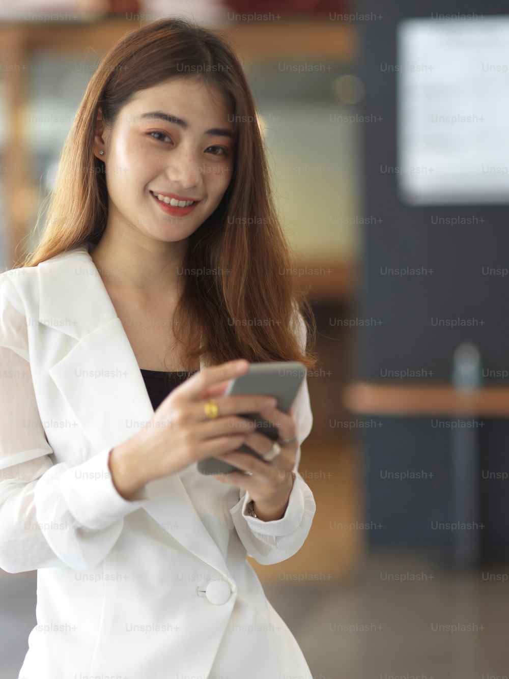 Portrait of female office worker smiling and looking into camera while relaxing with smartphone
