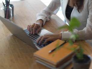 Cropped shot of female hands typing on laptop keyboard on wooden table with books and stationery