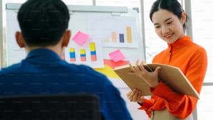 Young woman explains business data on white board in casual office room . The confident Asian businesswoman reports information progress of a business project to partner to determine market strategy .