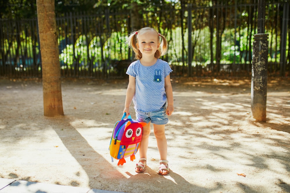 Menina adorável com mochila engraçada pronta para ir para creche, jardim de infância ou escola. Primeiro dia de conceito escolar