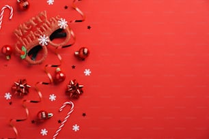 Maquette de carte d’invitation de fête de Noël. Verres festifs, décoration de boules de Noël, cannes de bonbon, confettis sur fond rouge. Mise à plat, vue de dessus, espace de copie