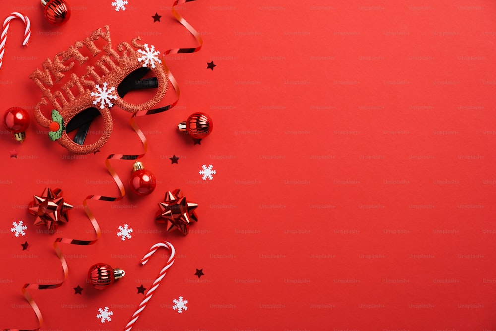Maquette de carte d’invitation de fête de Noël. Verres festifs, décoration de boules de Noël, cannes de bonbon, confettis sur fond rouge. Mise à plat, vue de dessus, espace de copie