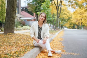 Schöne kaukasische Frau mittleren Alters mit kurzen Haaren sitzt im Herbst Herbst Straße im Freien. Junge Frau mit kurzem Haarschnitt in Freizeitkleidung im Park draußen. Kleine unvergessliche Momente des Lebens.