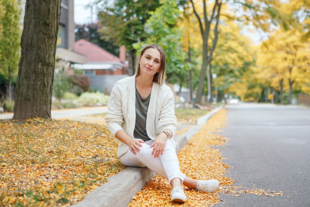 Beautiful middle age Caucasian woman with short hair sitting in autumn fall street outdoor. Young woman with short haircut in casual clothes in park outside. Little memorable moments of life.