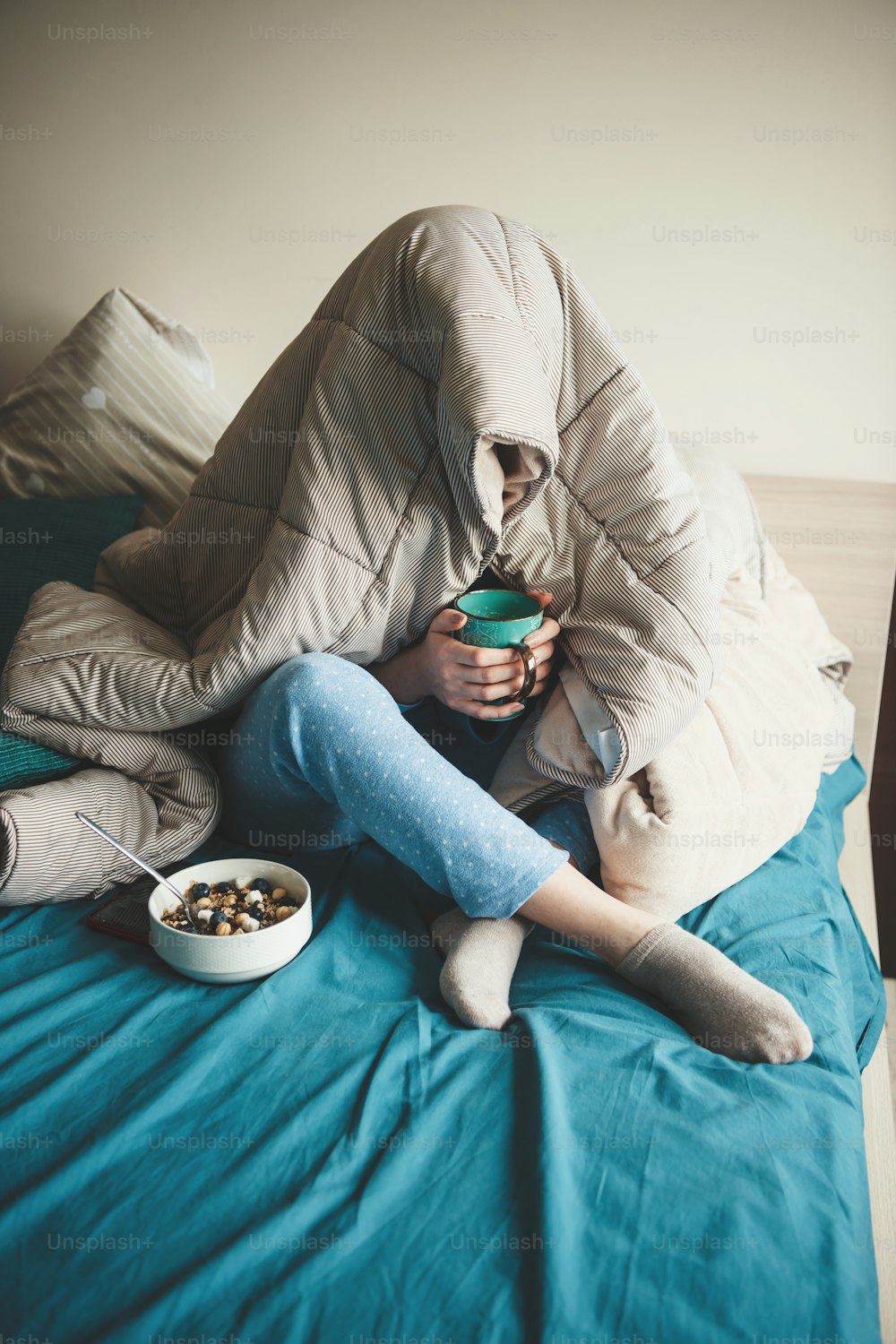 Donna caucasica a letto coperta da una trapunta sta bevendo un tè e mangiando cereali indossando un pigiama blu