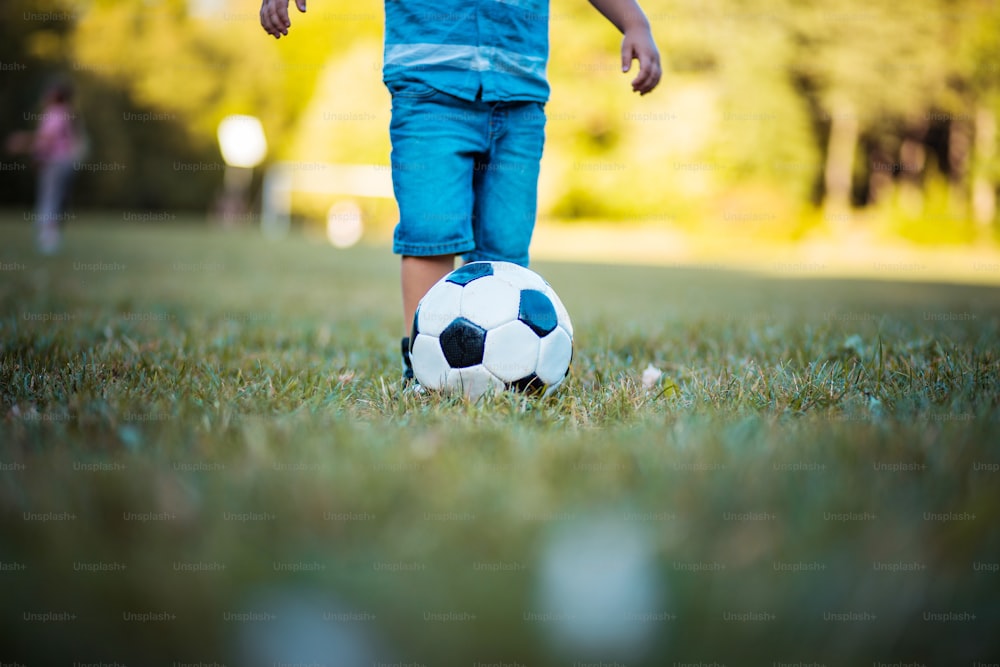 작은 축구 선수.  잔디밭에서 축구를 하는 어린 소년의 다리. 닫으십시오.