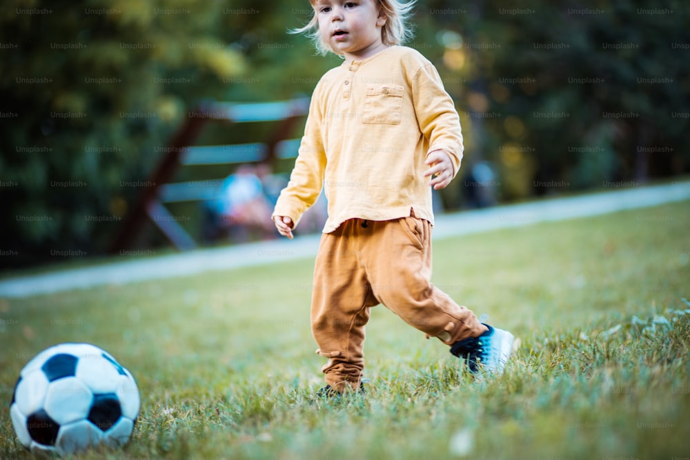 Tempo de futebol.  Garotinho jogando futebol no playground sozinho.