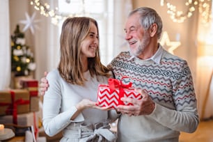 Happy senior man with young woman indoors at home at Christmas, holding present.