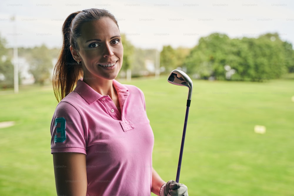 Waist-up portrait of a cute young golfer in a polo shirt smiling at the camera