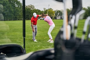 Golfista principiante concentrata che tenta di colpire la palla con una mazza di ferro aiutata dal suo allenatore