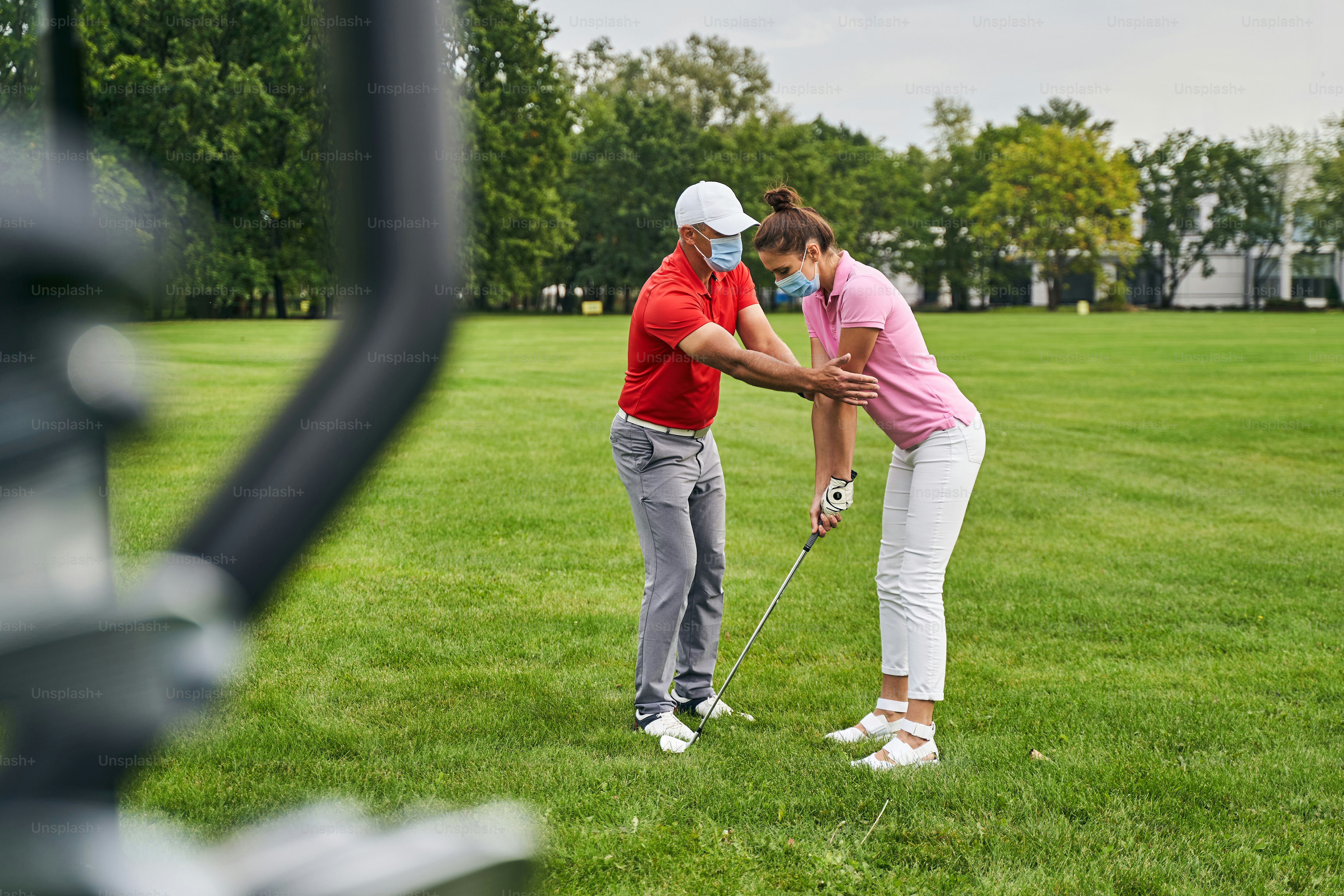 Focused woman golfer learning to get into a proper stance assisted by her personal coach