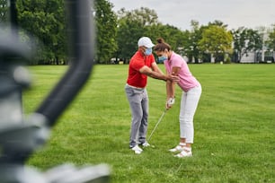 集中した女性ゴルファーは、パーソナルコーチの助けを借りて適切なスタンスを取ることを学びます