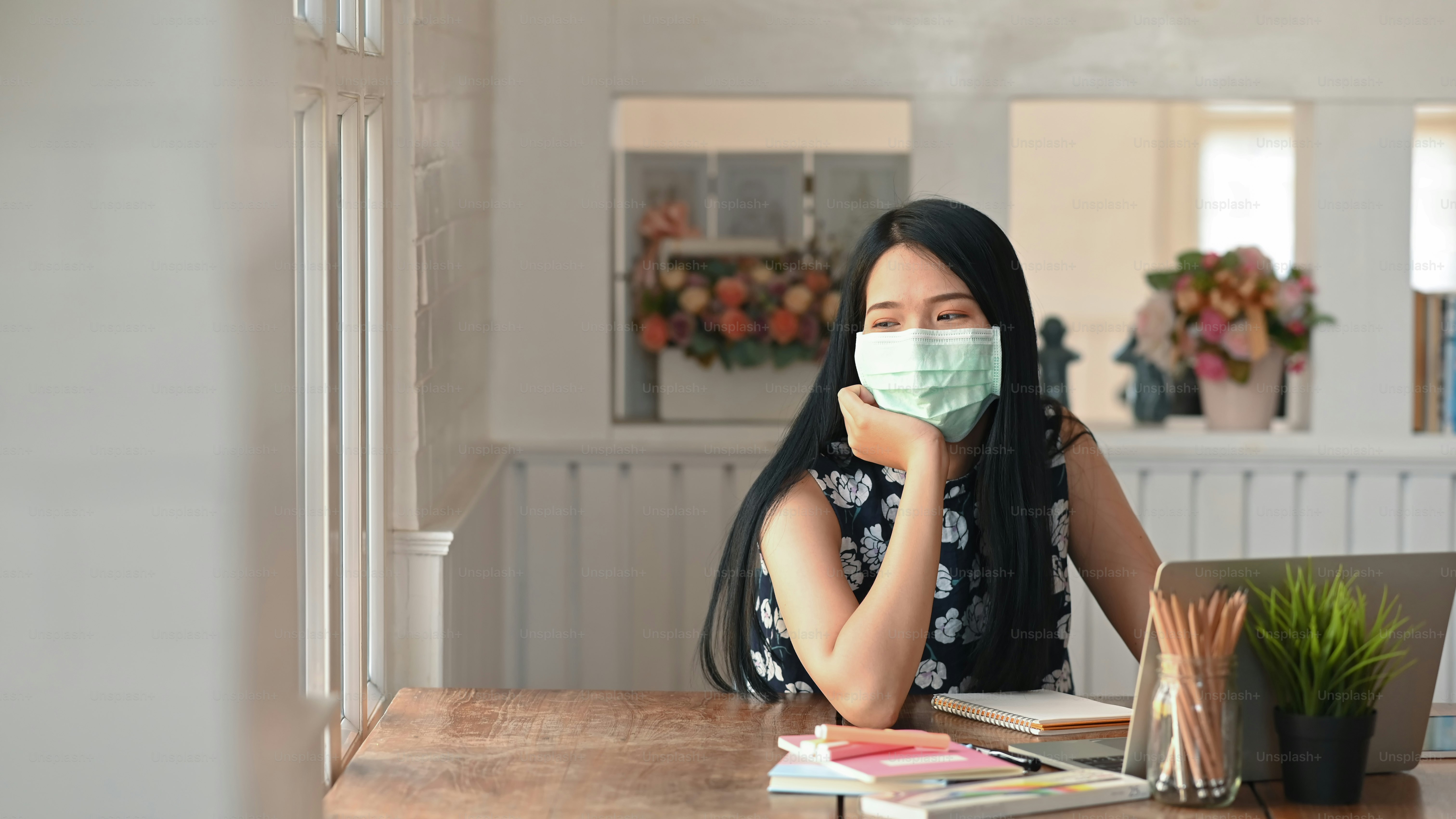 A young female wearing mask sitting in office while looking out the windows.