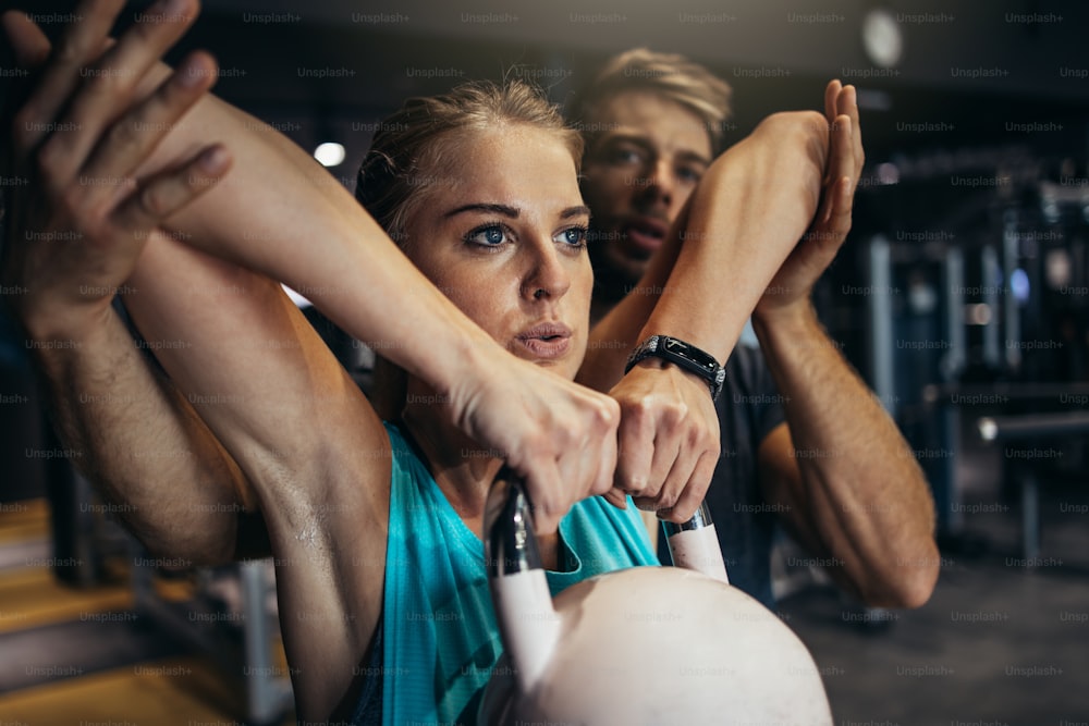 Young fit woman exercising in fitness gym with her personal fitness instructor or coach. Sport and healthy people lifestyle.