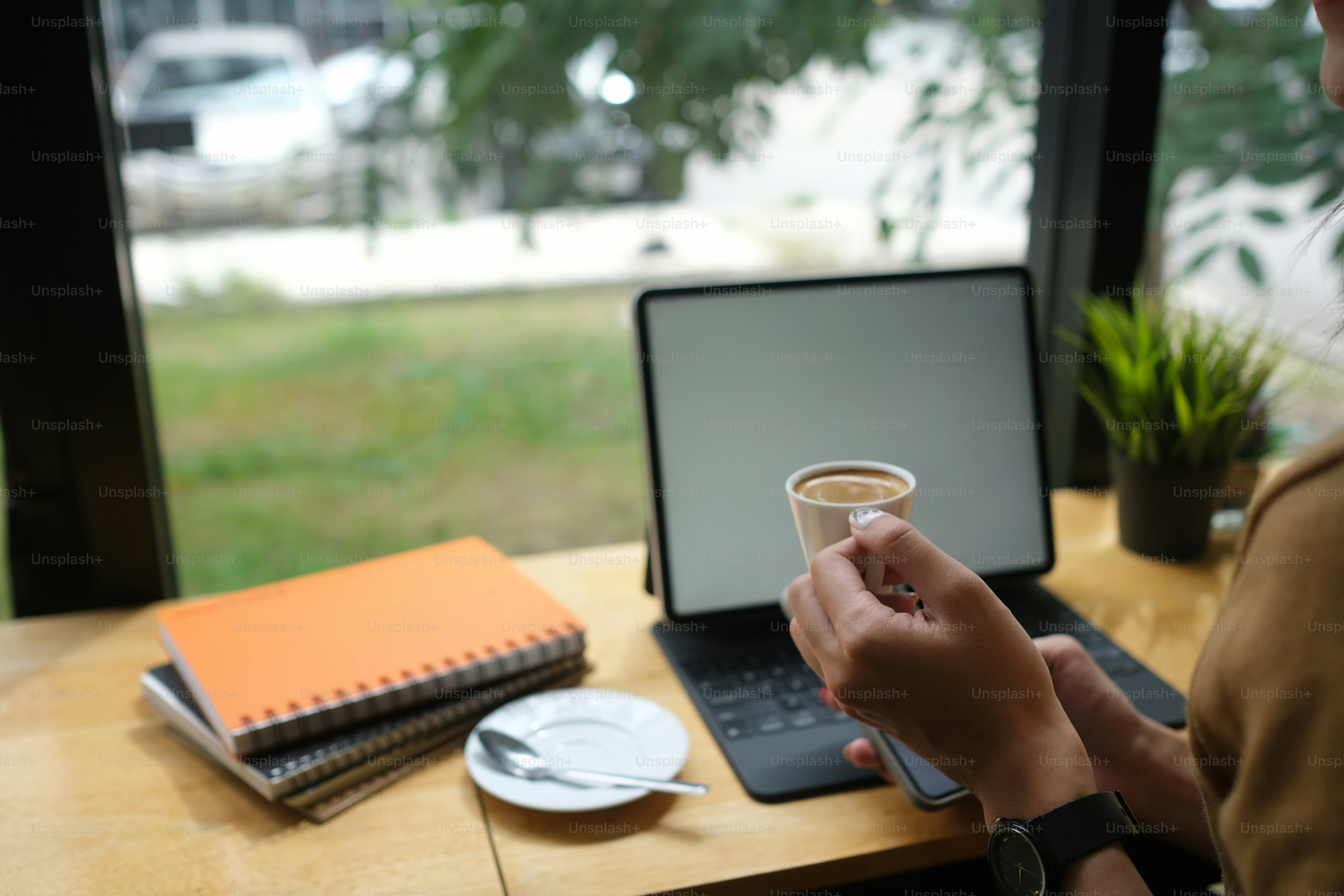 Abgeschnittene Aufnahme einer Bloggerin, die mit einem digitalen Tablet arbeitet und morgens Kaffee trinkt.