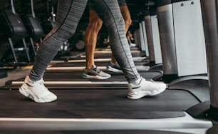 Mujer joven en forma y hombre corriendo en cinta de correr en gimnasio de fitness moderno. Primer plano sobre piernas en movimiento.