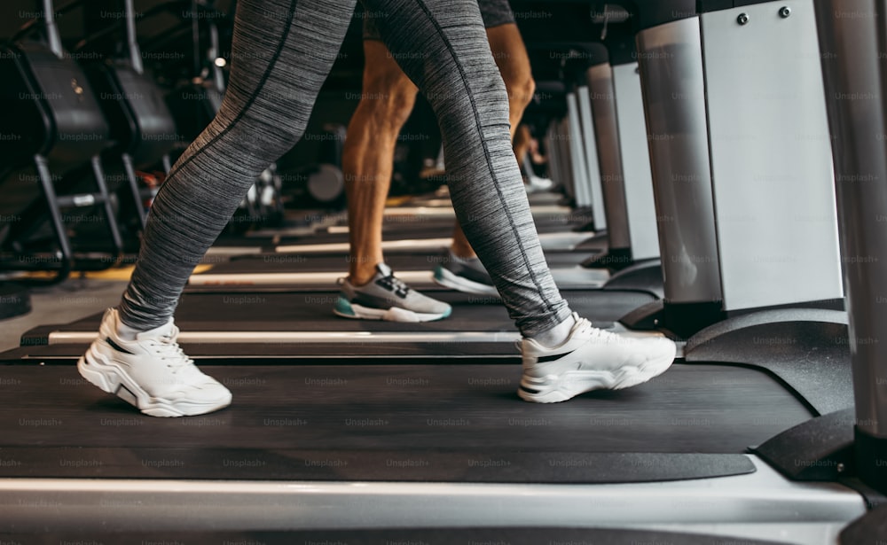 Giovane donna e uomo in forma che corrono sul tapis roulant nella moderna palestra di fitness. Scatto ravvicinato su gambe in movimento.