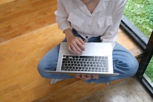 Cropped shot of young female hand working on laptop while sitting on the floor at home.