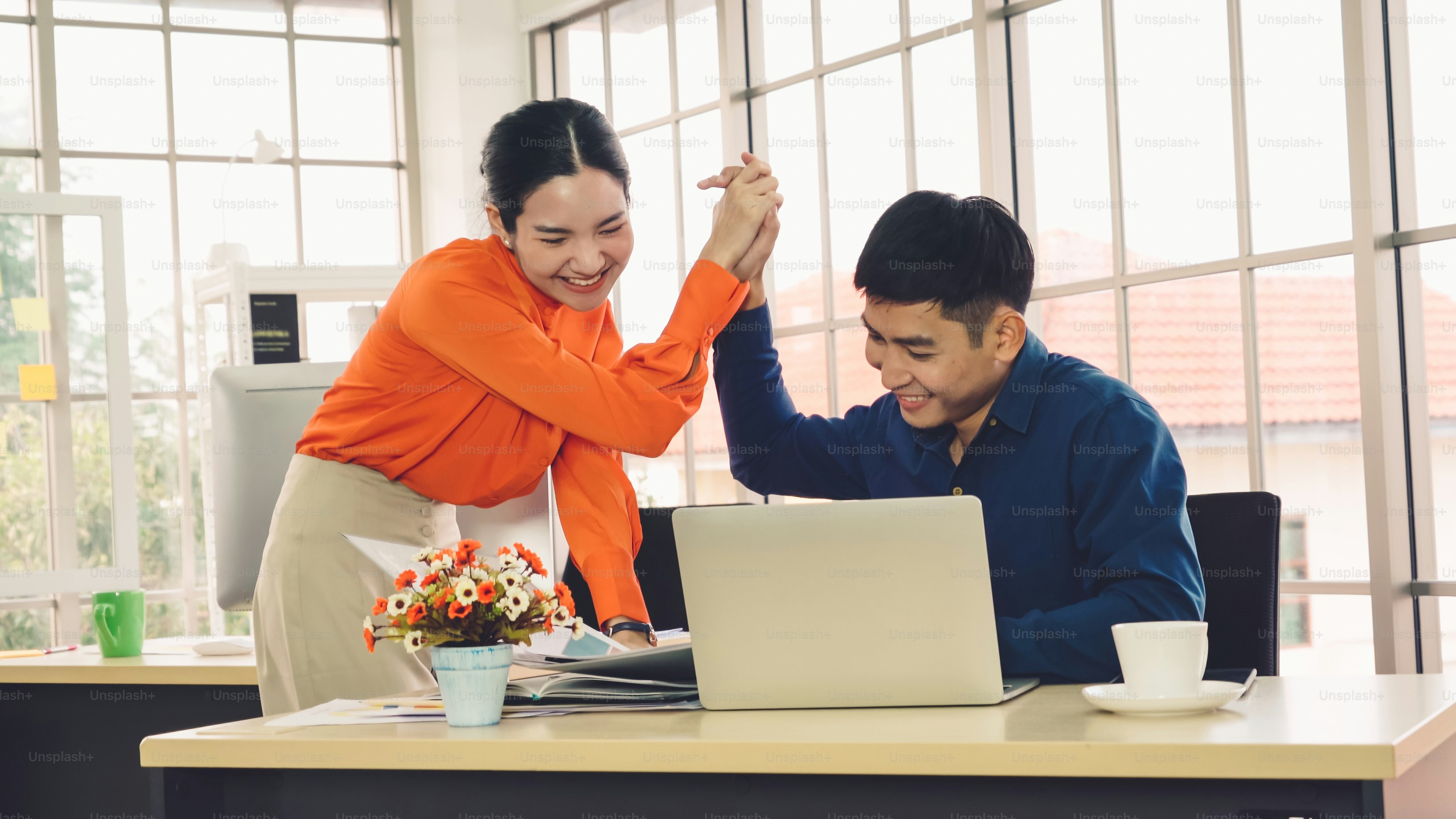 Two happy business people celebrate at office meeting room. Successful businessman congratulate project success with colleague at modern workplace while having conversation on financial data report.