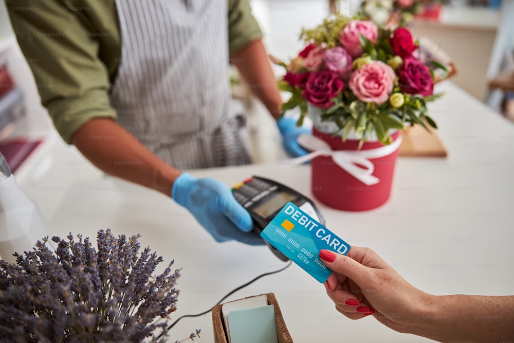 Buyer putting his bank card to a POS terminal while getting a flower bouquet in a pot on the table