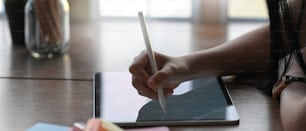 Close up view of young female designer hands using digital tablet with stylus on wooden desk.