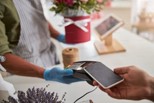 Der Kunde scannt sein Telefon an einem Blumenladen-Zahlungsterminal in der Hand eines Filialleiters