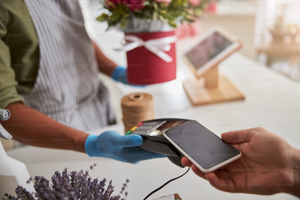 Customer scanning his phone on a flower shop payment terminal in the hand of a store manager
