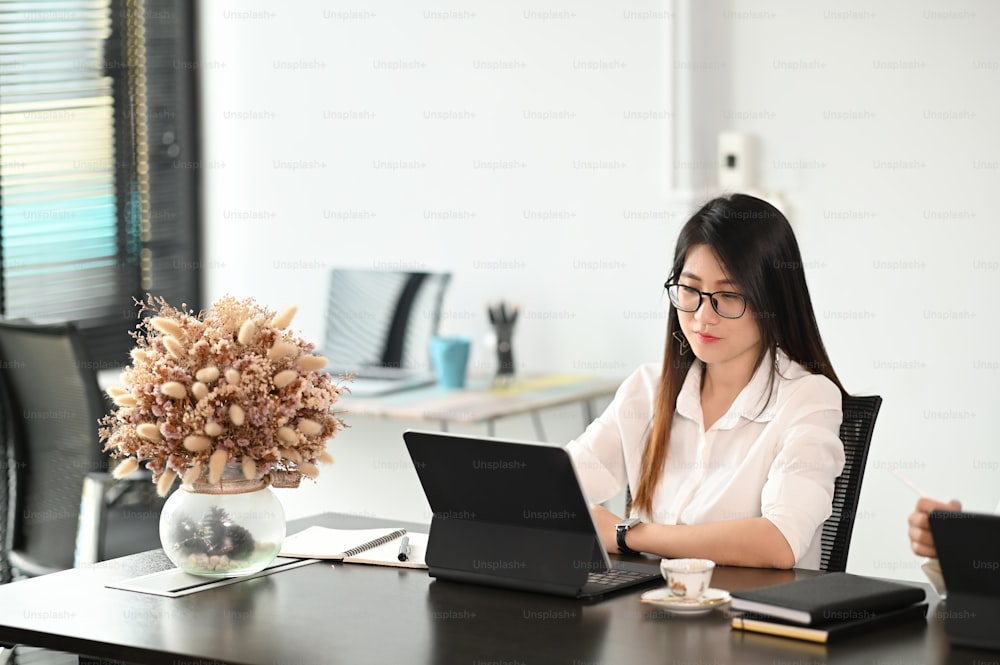 Confident woman using laptop computer and sitting in modern office.