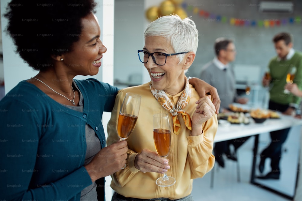 Cheerful mature businesswoman and her African American colleague toasting with Champagne while celebrating on a party in the office.