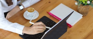 Vista superior de la mano femenina usando una tableta digital con un lápiz óptico en una mesa de madera en la cafetería