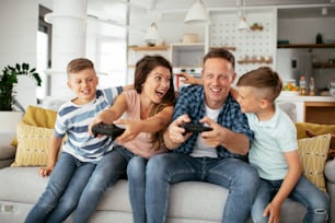 Husband and wife playing video games with joysticks in living room. Loving couple are playing video games with kids at home"t