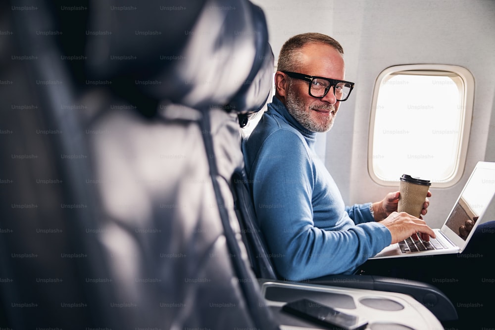 Smiling Caucasian airline passenger with a paper cup of coffee and a laptop looking ahead