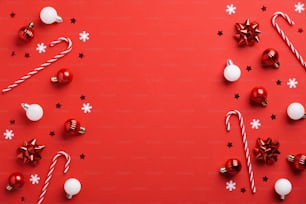 Fond de Noël rouge avec décoration de boules de Noël rouges et blanches, cannes de bonbon et confettis. Modèle de carte postale de Noël, maquette de bannière.