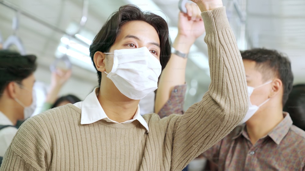 Young man wearing face mask travels on crowded subway train . Coronavirus disease or COVID 19 pandemic outbreak and urban lifestyle problem in rush hour concept .