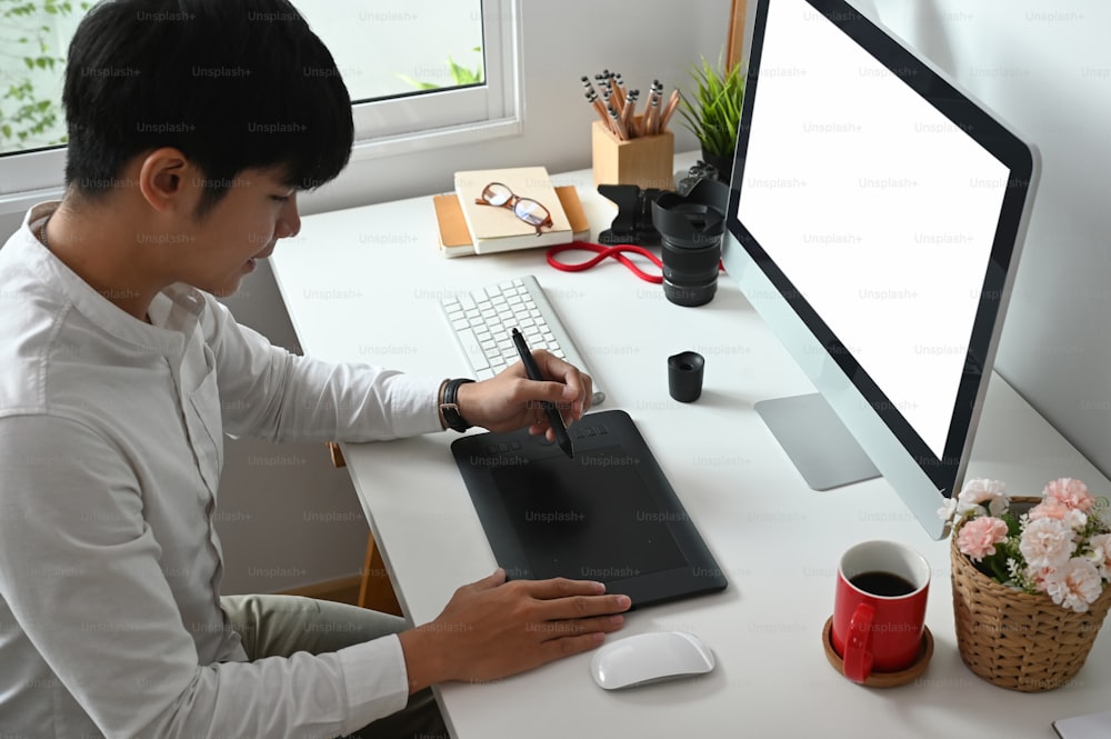Young Asian graphic designer working on computor and graphics tablet in his working space.