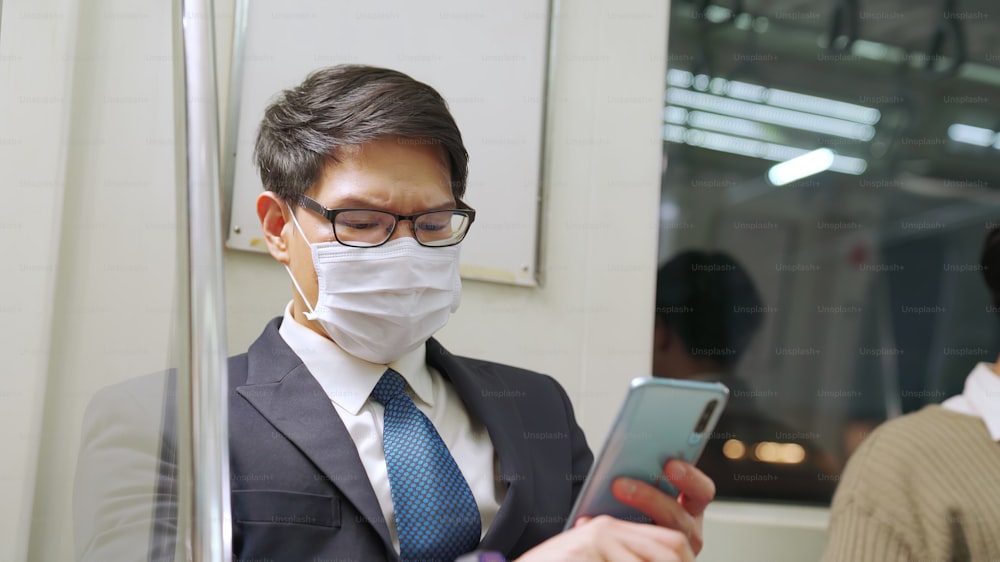 Viaggiatore che indossa una maschera facciale mentre utilizza il telefono cellulare sul treno pubblico. Malattia da coronavirus o epidemia di pandemia COVID 19 e problema dello stile di vita della città urbana nel concetto di pendolarismo dell'ora di punta.