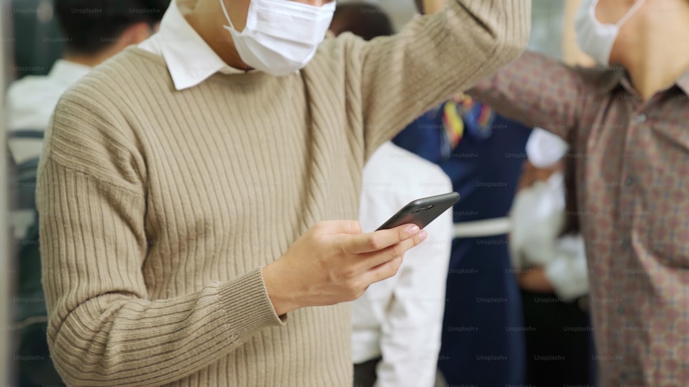 대중 열차에서 휴대 전화를 사용하는 동안 안면 마스크를 착용 한 여행자. 코로나바이러스 질병 또는 COVID 19 전염병 발생 및 러시아워 통근 개념의 도시 도시 생활 방식 문제.