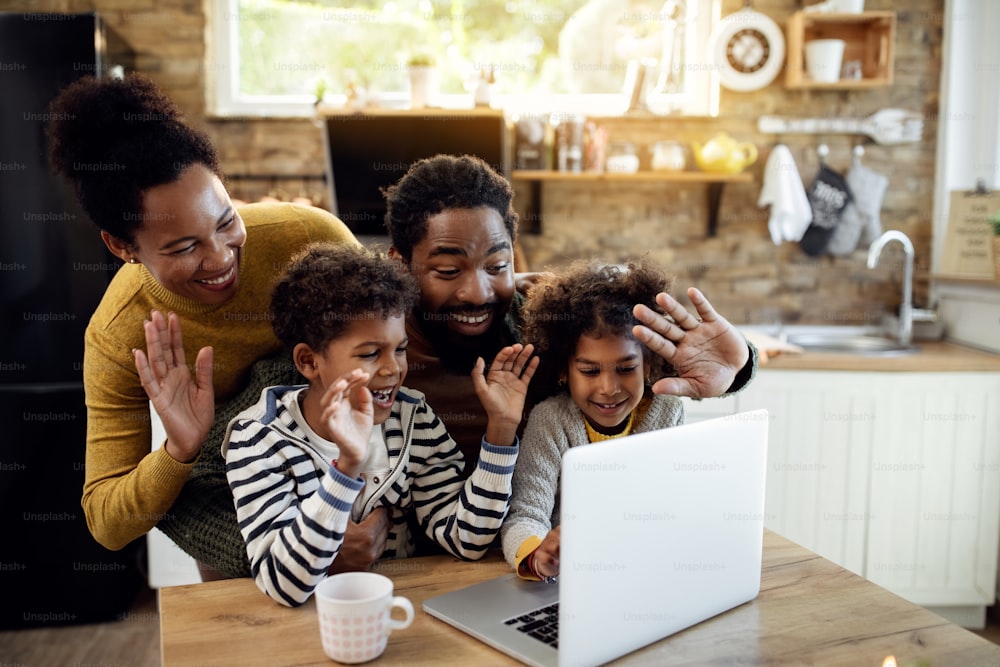 Happy black family using computer and greeting someone while making video call at home.