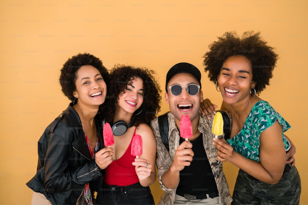 Portrait of multi-ethnic group of friends having fun and enjoying summertime while eating ice cream against yellow background.