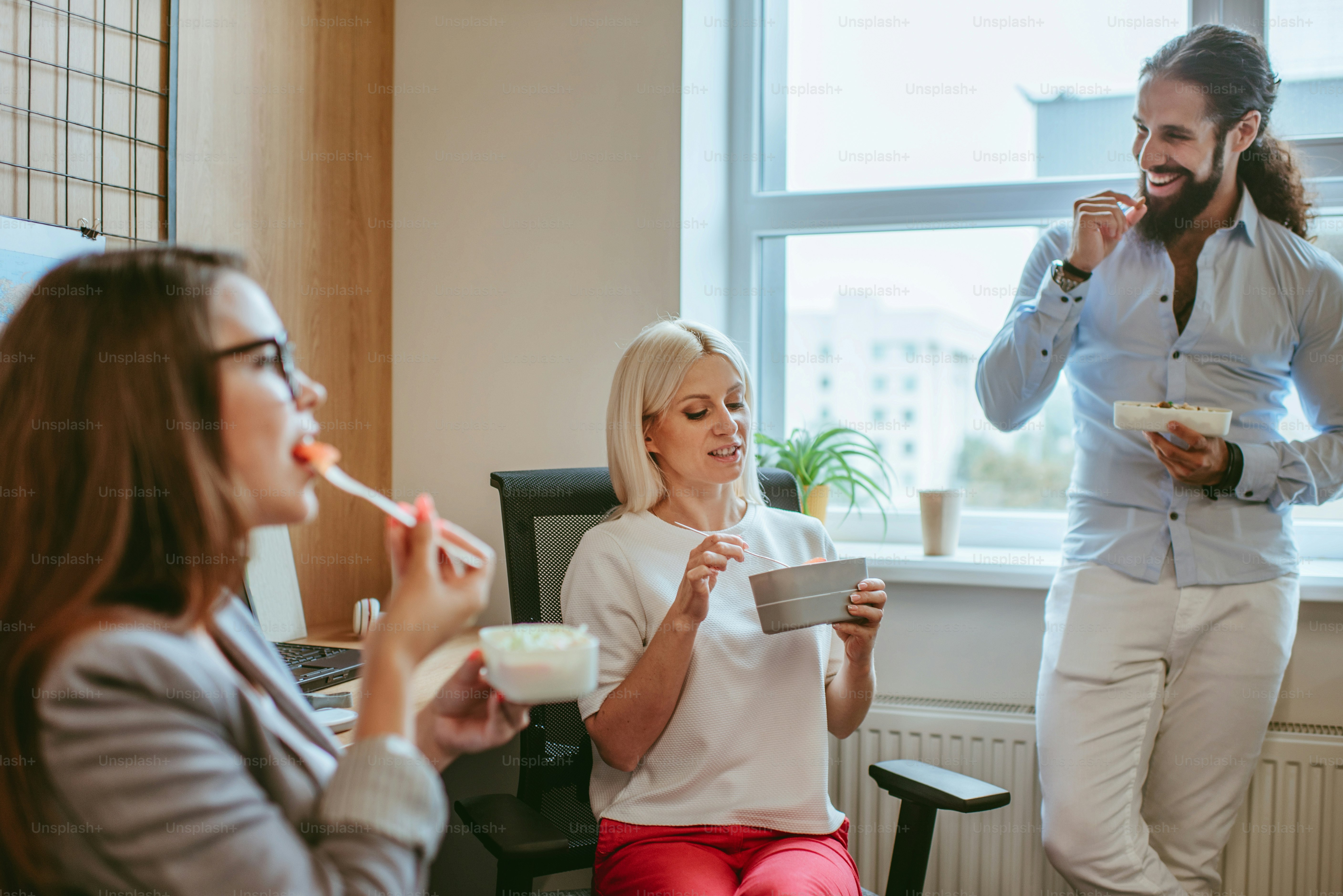 A lunch time in the office. Three business people having their lunch from lunch boxes in the modern workspace.