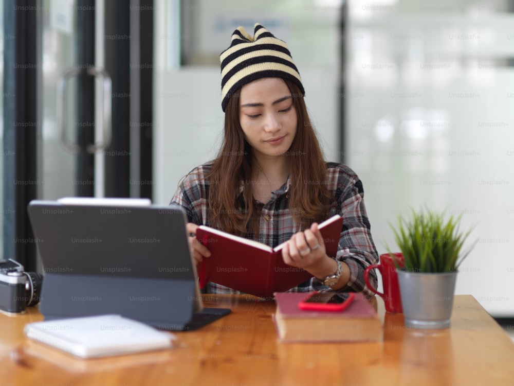 Portrait of female teenager doing assignment with book and tablet in cafe