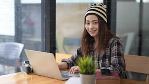 Portrait of female teenager working with laptop on wooden table in cafe