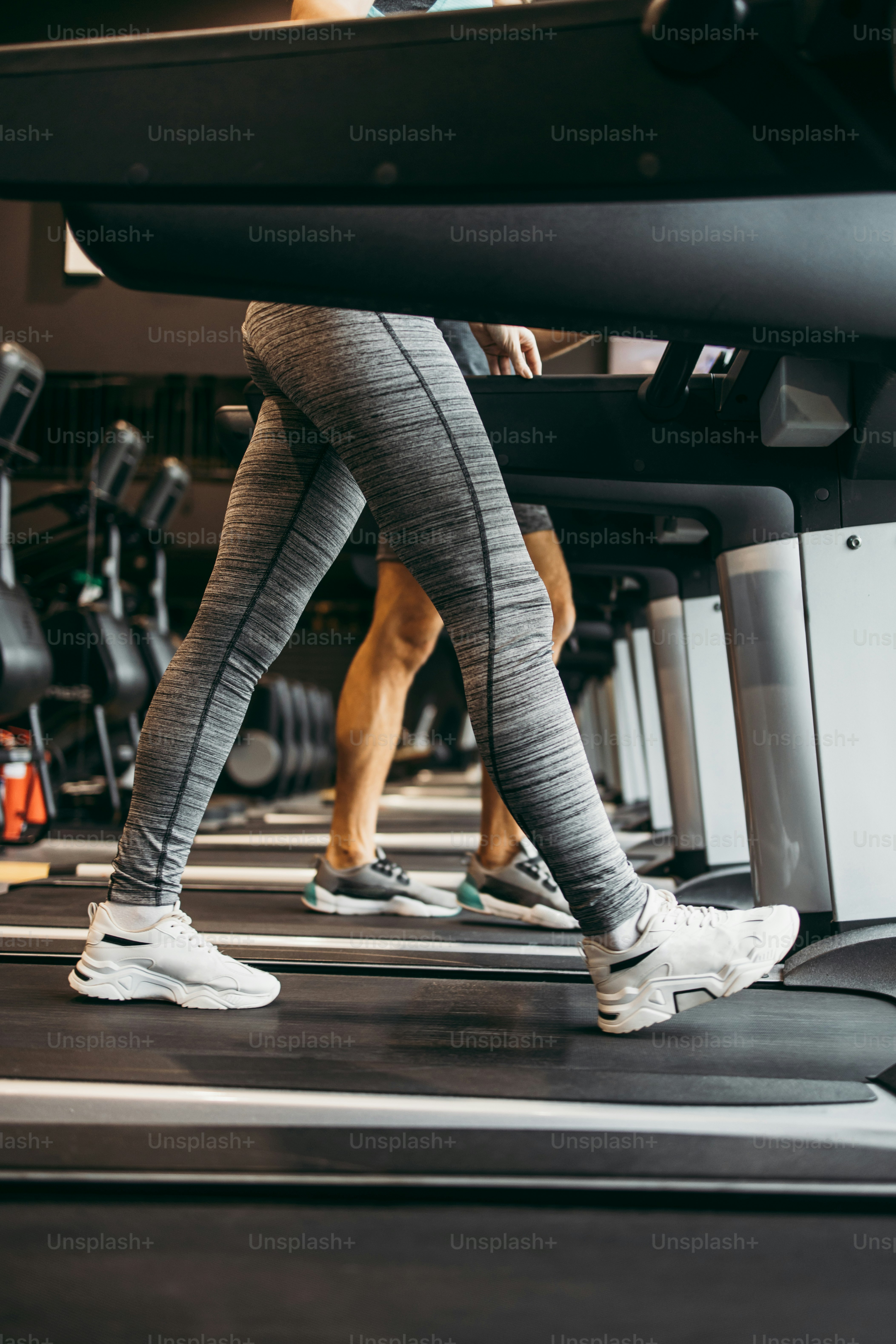 Young fit woman and man running on treadmill in modern fitness gym. Close up shot on moving legs.
