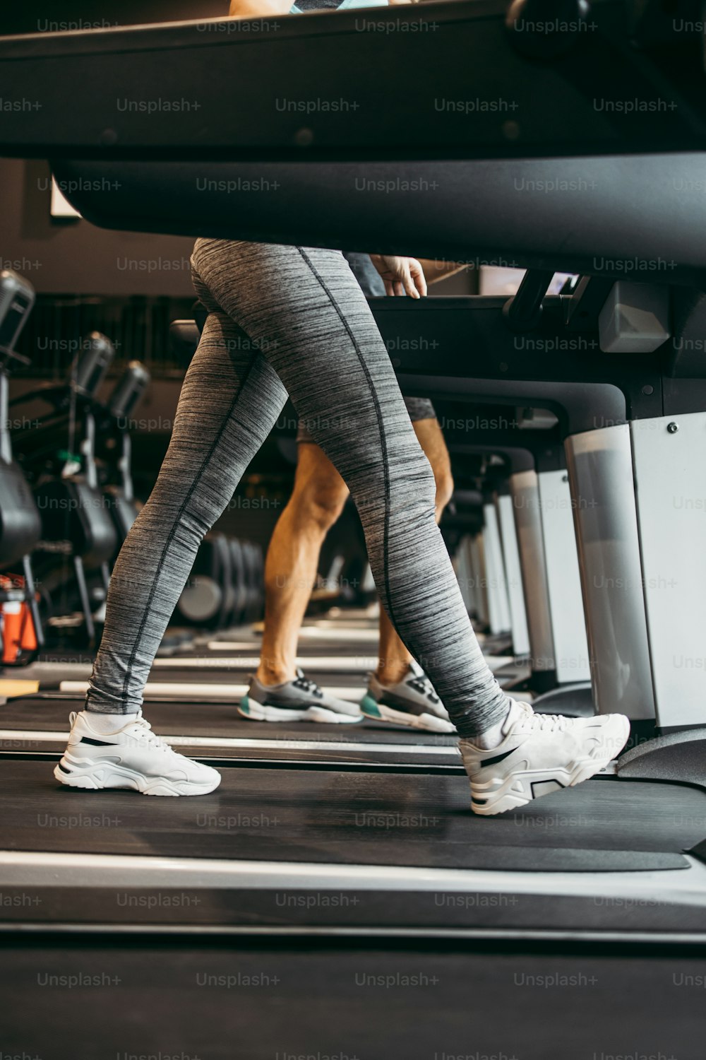 Young fit woman and man running on treadmill in modern fitness gym