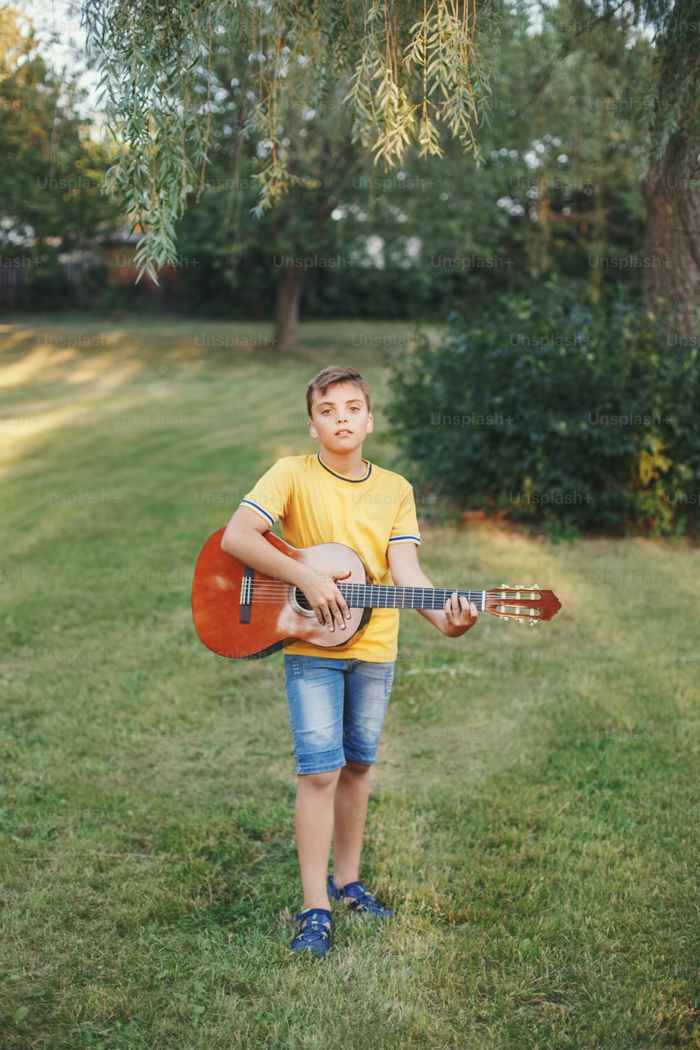 Hard of hearing preteen boy playing guitar outdoor. Child with hearing aids in ears playing music and singing song in park. Hobby art activity for children kids. Authentic childhood moment.