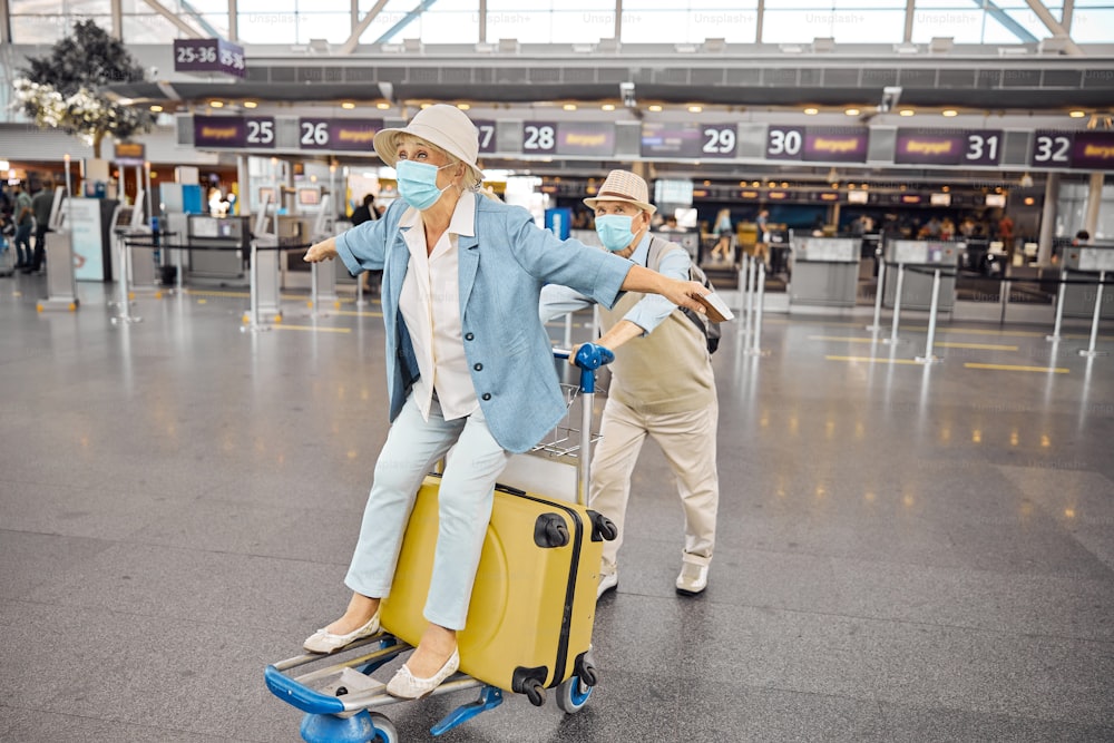 Senior woman with outstretched arms enjoying her ride on a luggage trolley at the airport terminal