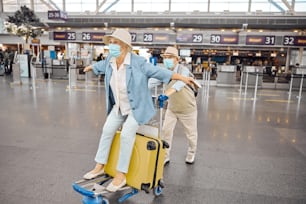 Senior woman with outstretched arms enjoying her ride on a luggage trolley at the airport terminal